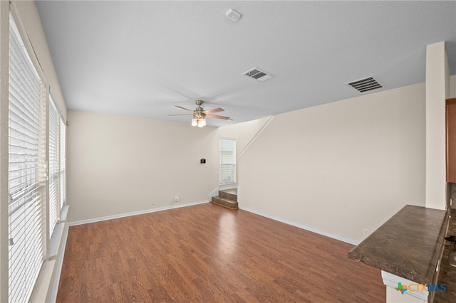 unfurnished living room featuring a ceiling fan, wood finished floors, visible vents, and baseboards