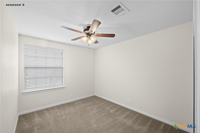 carpeted spare room featuring visible vents, baseboards, and a ceiling fan