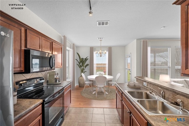 kitchen with light tile patterned floors, a sink, decorative backsplash, appliances with stainless steel finishes, and brown cabinets