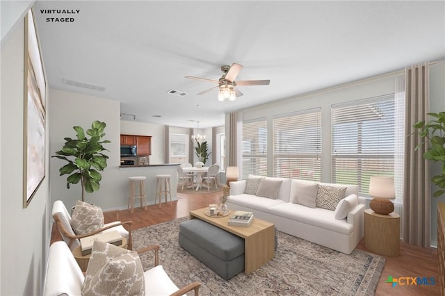 living room with ceiling fan with notable chandelier, wood finished floors, and visible vents