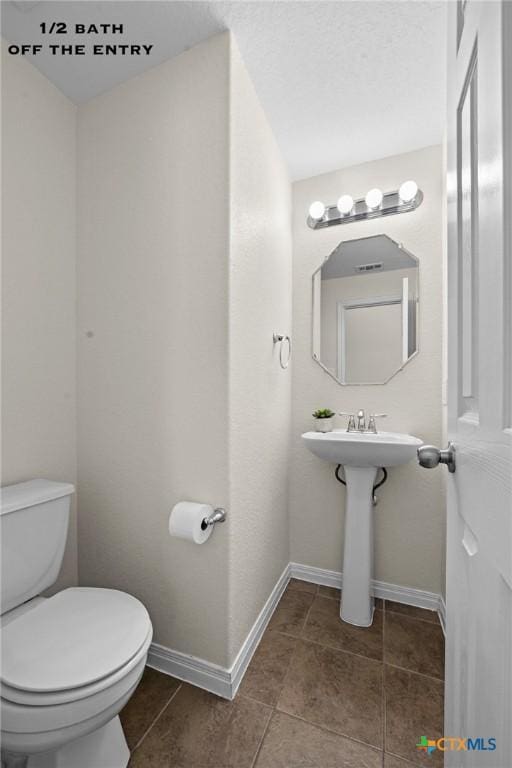 half bath featuring tile patterned flooring, toilet, and baseboards