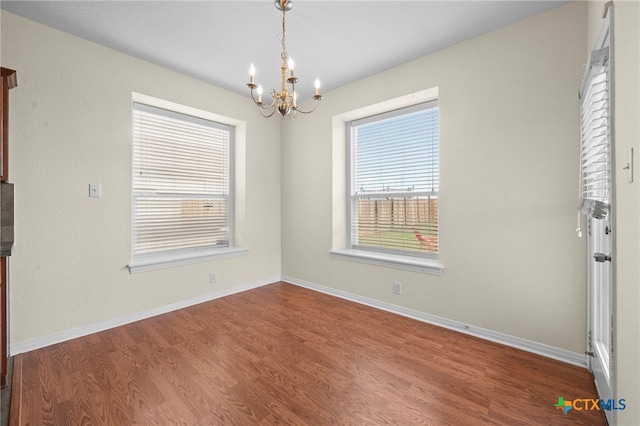 unfurnished room featuring wood finished floors, baseboards, and a chandelier