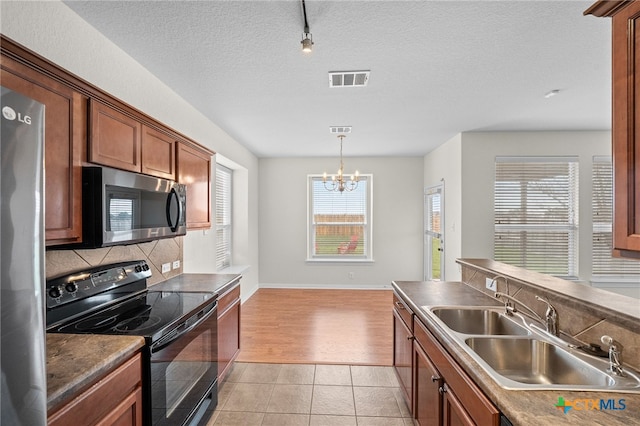 kitchen featuring light tile patterned floors, a sink, stainless steel appliances, brown cabinets, and backsplash