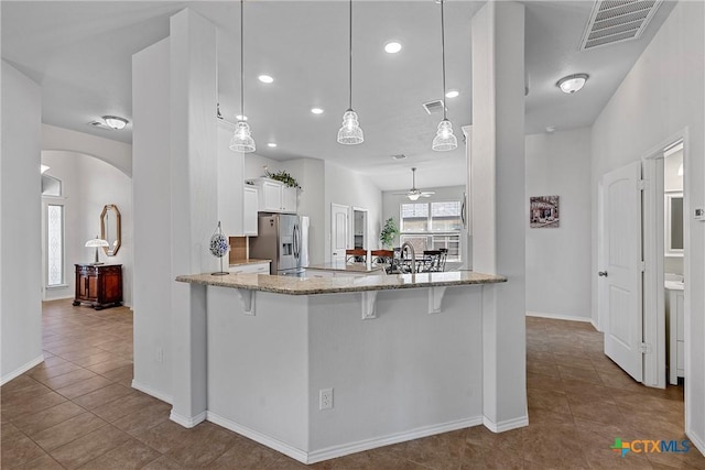 kitchen featuring kitchen peninsula, stainless steel fridge, pendant lighting, white cabinets, and a breakfast bar