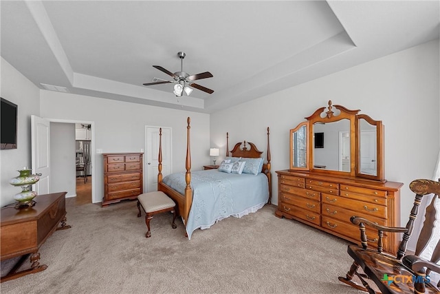 bedroom featuring ceiling fan, a tray ceiling, and light carpet