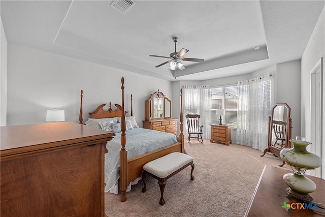 carpeted bedroom with ceiling fan and a tray ceiling