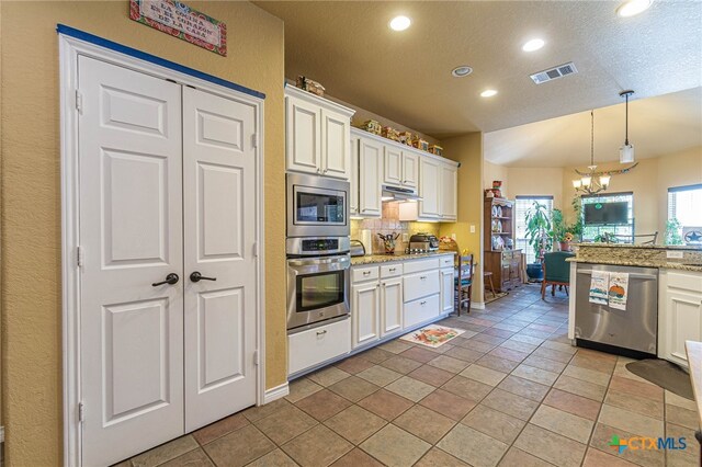 kitchen with light stone countertops, tasteful backsplash, a chandelier, white cabinets, and appliances with stainless steel finishes