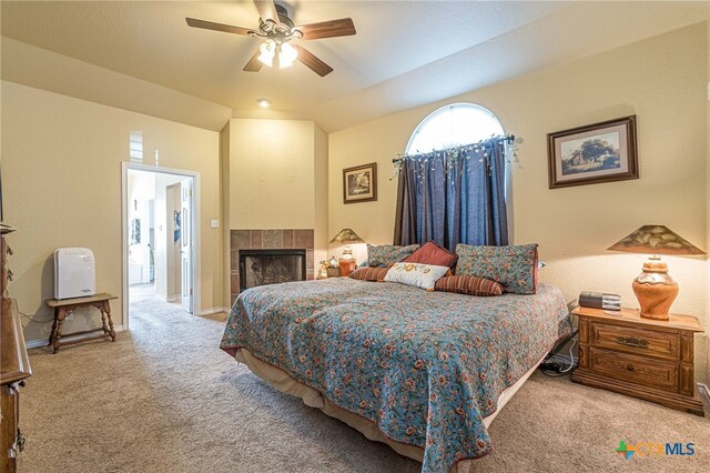 bedroom featuring ceiling fan, light colored carpet, a tiled fireplace, and vaulted ceiling