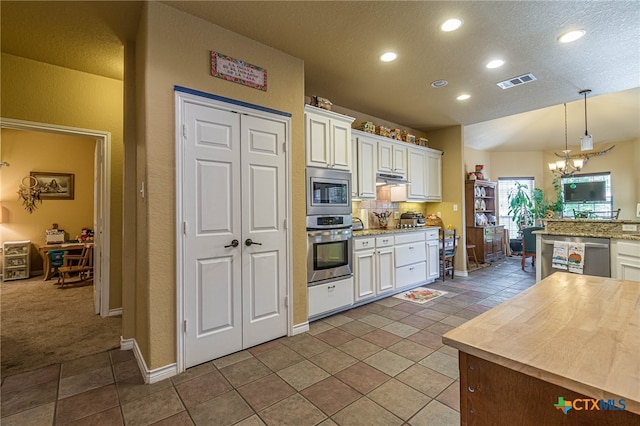 kitchen with appliances with stainless steel finishes, white cabinetry, and hanging light fixtures