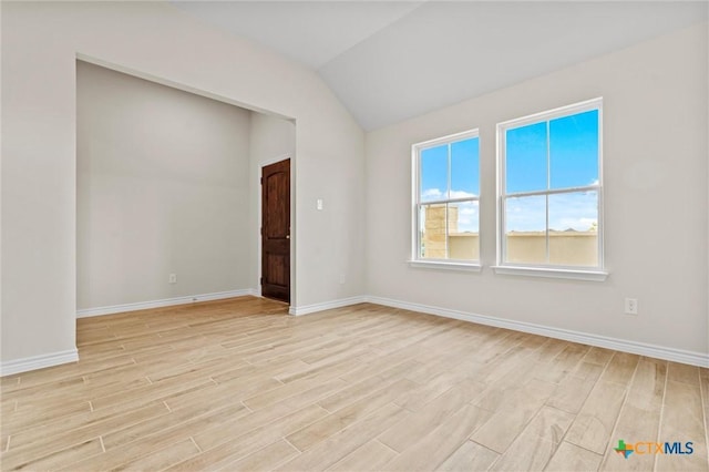 empty room with light wood-style floors, vaulted ceiling, and baseboards