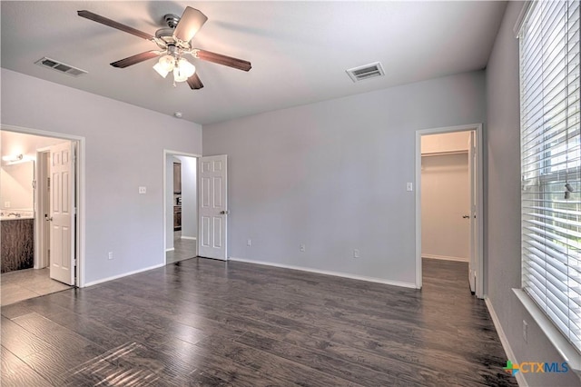 unfurnished bedroom featuring ensuite bathroom, a walk in closet, ceiling fan, dark wood-type flooring, and a closet