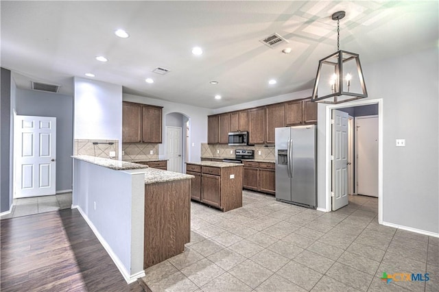 kitchen with an inviting chandelier, hanging light fixtures, stainless steel appliances, light stone counters, and tasteful backsplash