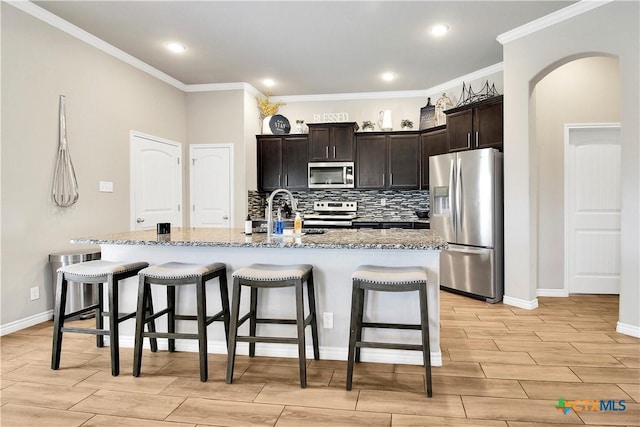 kitchen with an island with sink, sink, a breakfast bar area, stainless steel appliances, and dark brown cabinets