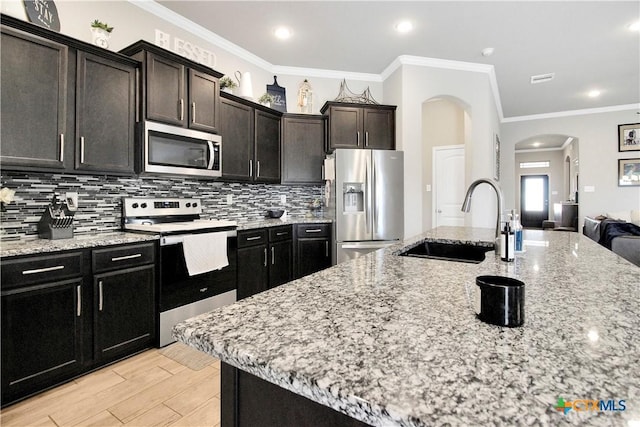 kitchen with a kitchen island with sink, sink, backsplash, and appliances with stainless steel finishes