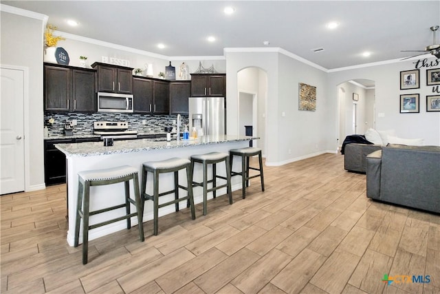 kitchen with a breakfast bar, ceiling fan, stainless steel appliances, light hardwood / wood-style floors, and a center island with sink