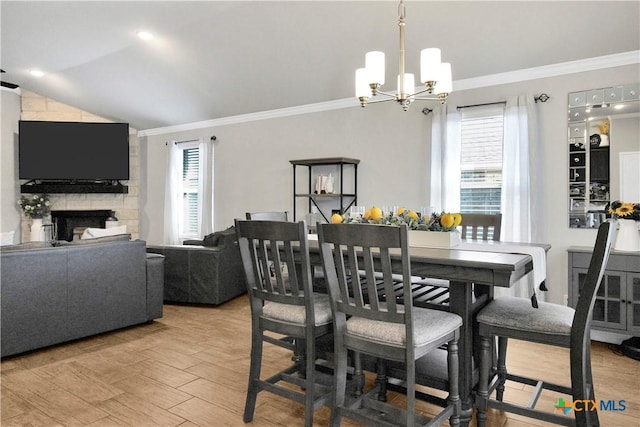 dining space featuring lofted ceiling, a stone fireplace, light hardwood / wood-style floors, and crown molding