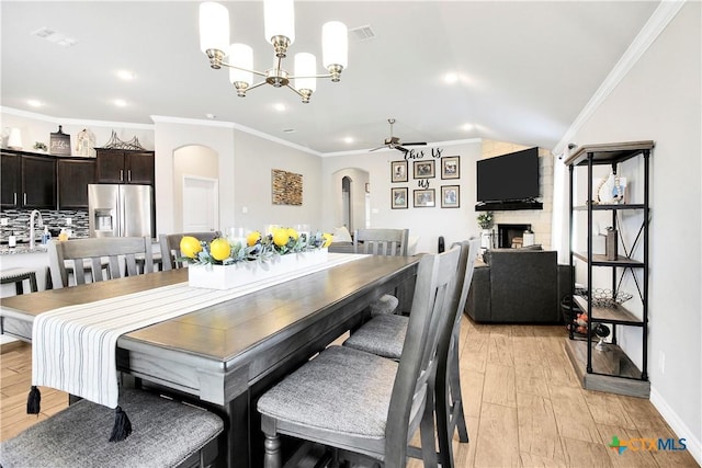 dining area with crown molding, a fireplace, ceiling fan with notable chandelier, and light wood-type flooring