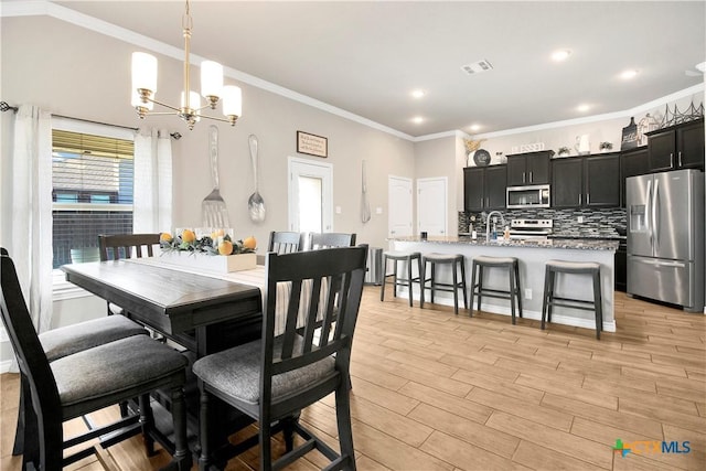 dining room featuring crown molding, sink, a chandelier, and light hardwood / wood-style floors