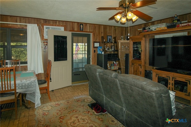 living room featuring ceiling fan, a textured ceiling, plenty of natural light, and wood walls