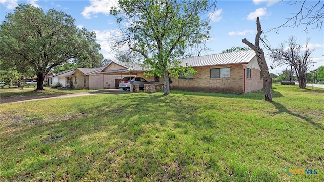 single story home featuring brick siding, metal roof, an attached carport, driveway, and a front yard