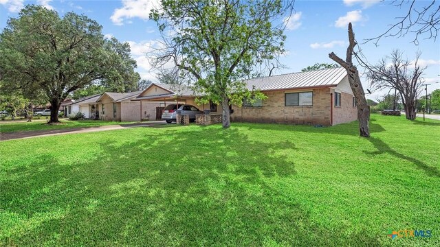 ranch-style house featuring brick siding, metal roof, an attached carport, driveway, and a front yard