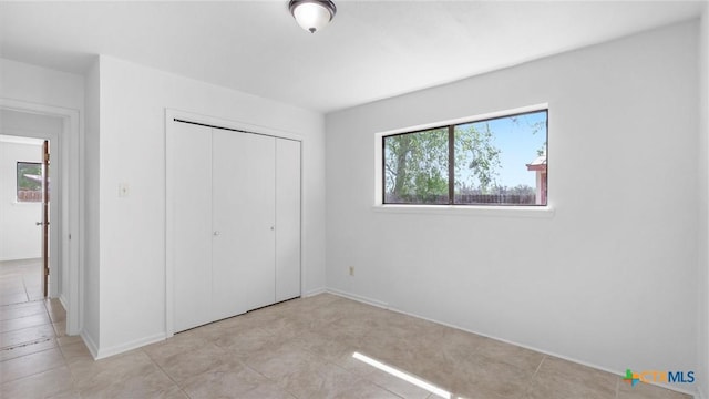 unfurnished bedroom with baseboards, light tile patterned flooring, and a closet