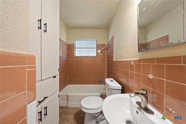 full bathroom with tile walls, sink, hardwood / wood-style flooring, toilet, and tiled shower / bath