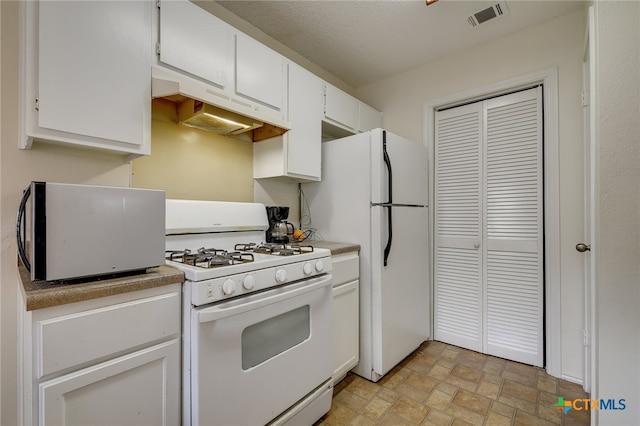 kitchen featuring visible vents, stone finish floor, under cabinet range hood, white cabinetry, and white appliances