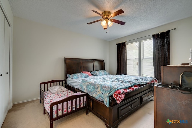 bedroom featuring baseboards, ceiling fan, light carpet, a closet, and a textured ceiling