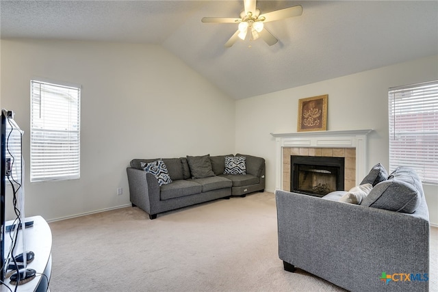 carpeted living area with a wealth of natural light, ceiling fan, a tile fireplace, and vaulted ceiling