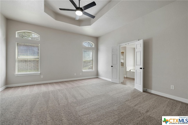 unfurnished bedroom with light colored carpet, a raised ceiling, multiple windows, and ceiling fan