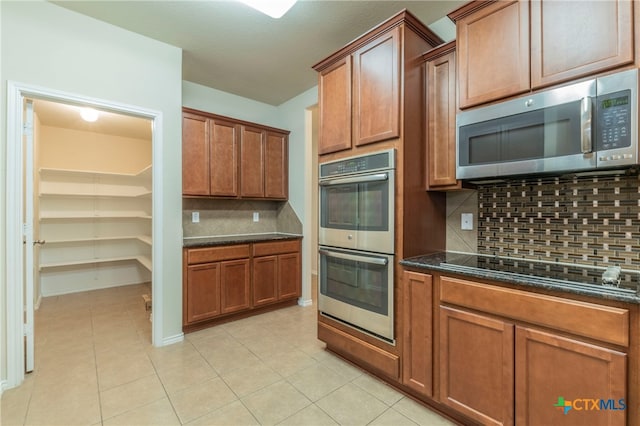 kitchen with dark stone counters, light tile patterned floors, decorative backsplash, and appliances with stainless steel finishes