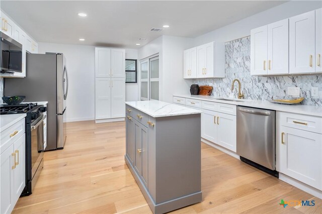 kitchen with appliances with stainless steel finishes, a center island, backsplash, white cabinetry, and a sink