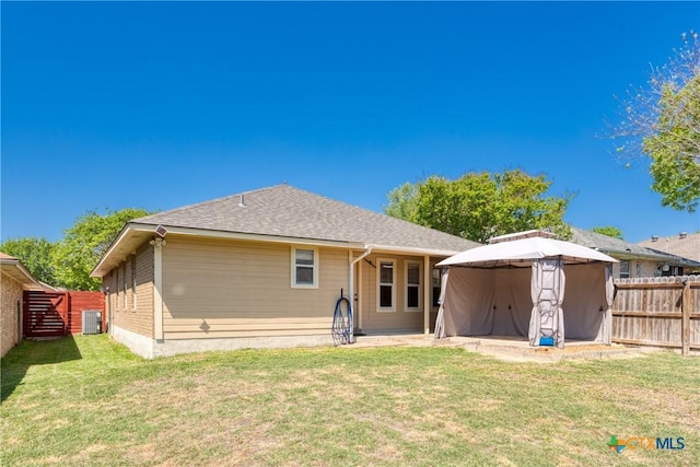 back of house featuring a fenced backyard, a gazebo, a lawn, and a shingled roof