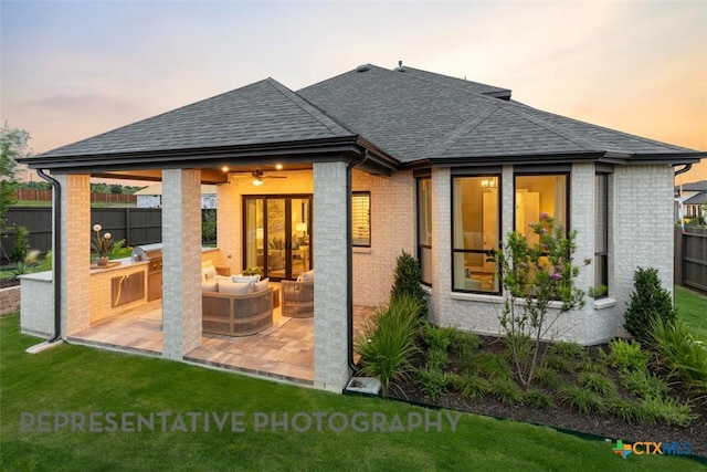 221 Dycus Bnd, Liberty Hill, TX 78642 - back of house at dusk featuring roof with shingles, brick siding, area for grilling, and a patio