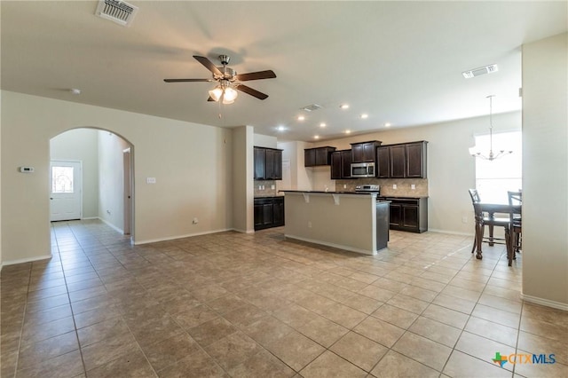 kitchen with ceiling fan with notable chandelier, a kitchen breakfast bar, light tile patterned floors, an island with sink, and tasteful backsplash