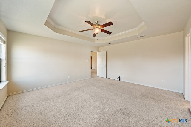 carpeted empty room with a raised ceiling, ceiling fan, and ornamental molding