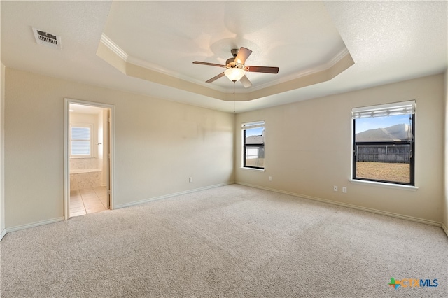 unfurnished room featuring a raised ceiling, ceiling fan, light colored carpet, and ornamental molding