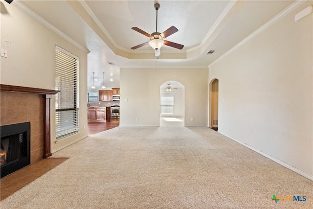 unfurnished living room with carpet flooring, a tray ceiling, ceiling fan, crown molding, and a fireplace