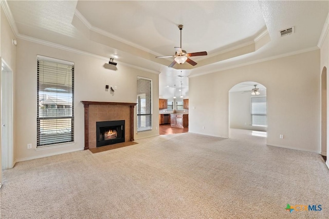 unfurnished living room featuring a tiled fireplace, light colored carpet, ornamental molding, and a raised ceiling