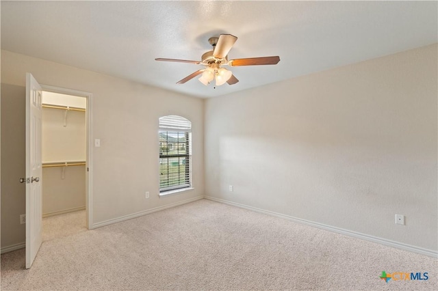 unfurnished bedroom with light carpet, a spacious closet, a closet, and ceiling fan