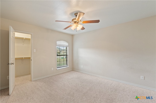 unfurnished bedroom with a closet, a spacious closet, ceiling fan, and light colored carpet