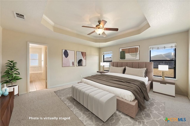 carpeted bedroom with crown molding, connected bathroom, a tray ceiling, and multiple windows