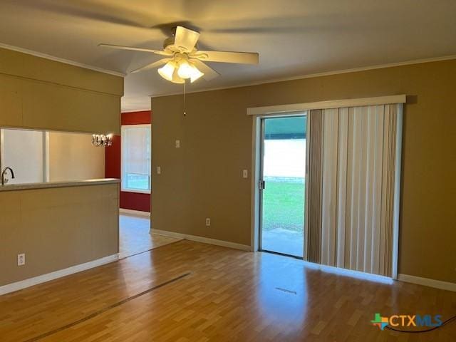 empty room with baseboards, crown molding, ceiling fan with notable chandelier, and light wood-type flooring
