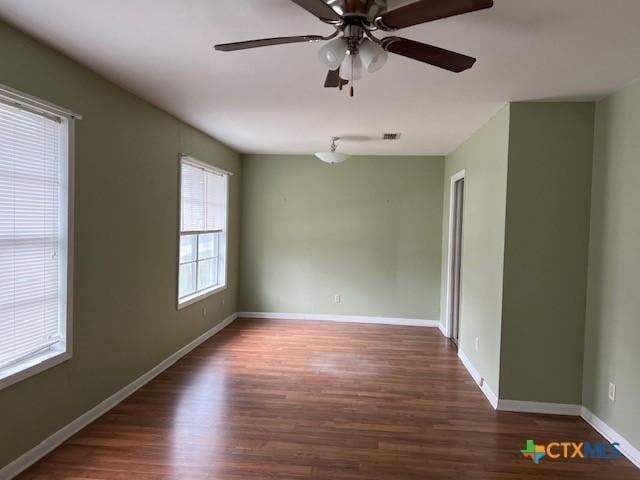 empty room with wood finished floors, visible vents, a ceiling fan, and baseboards