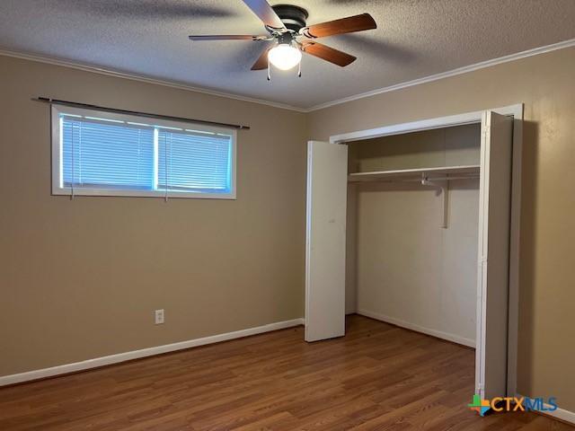 unfurnished bedroom with crown molding, wood finished floors, a textured ceiling, ceiling fan, and baseboards