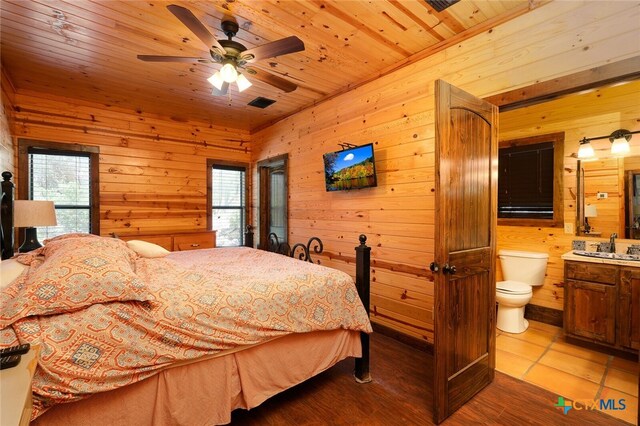 bedroom featuring ensuite bath, wooden walls, multiple windows, and ceiling fan