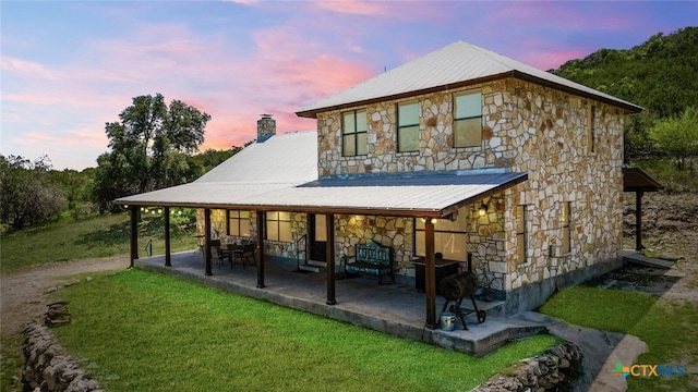 back house at dusk featuring a lawn and a patio area