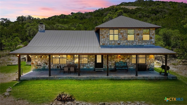 back house at dusk featuring a lawn and a patio area