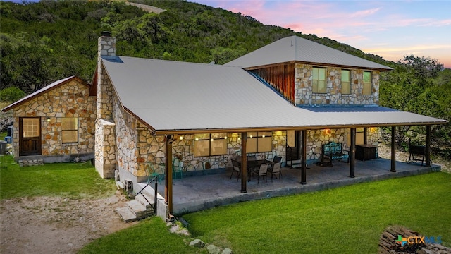 back house at dusk featuring a yard and a patio area